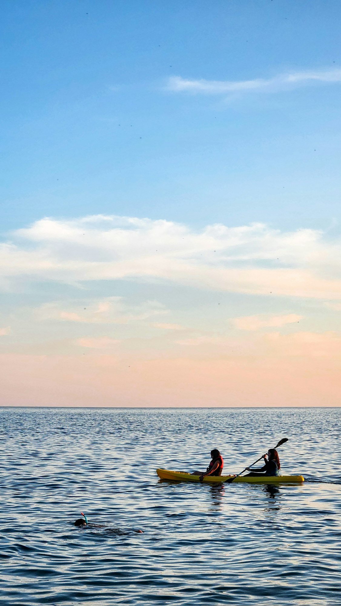 Deux personnes en kayak au coucher du soleil, sur une mer calme