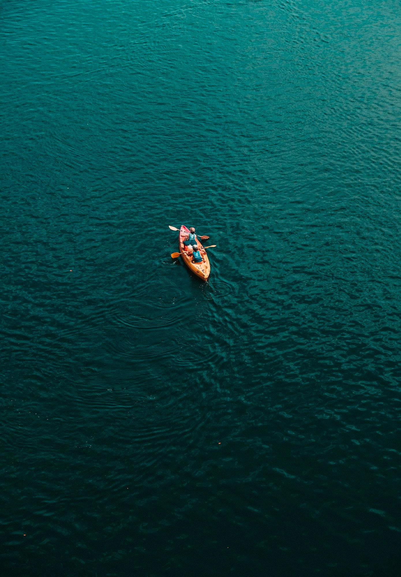 Un kayak biplace orange au milieu d’une mer bleu profond