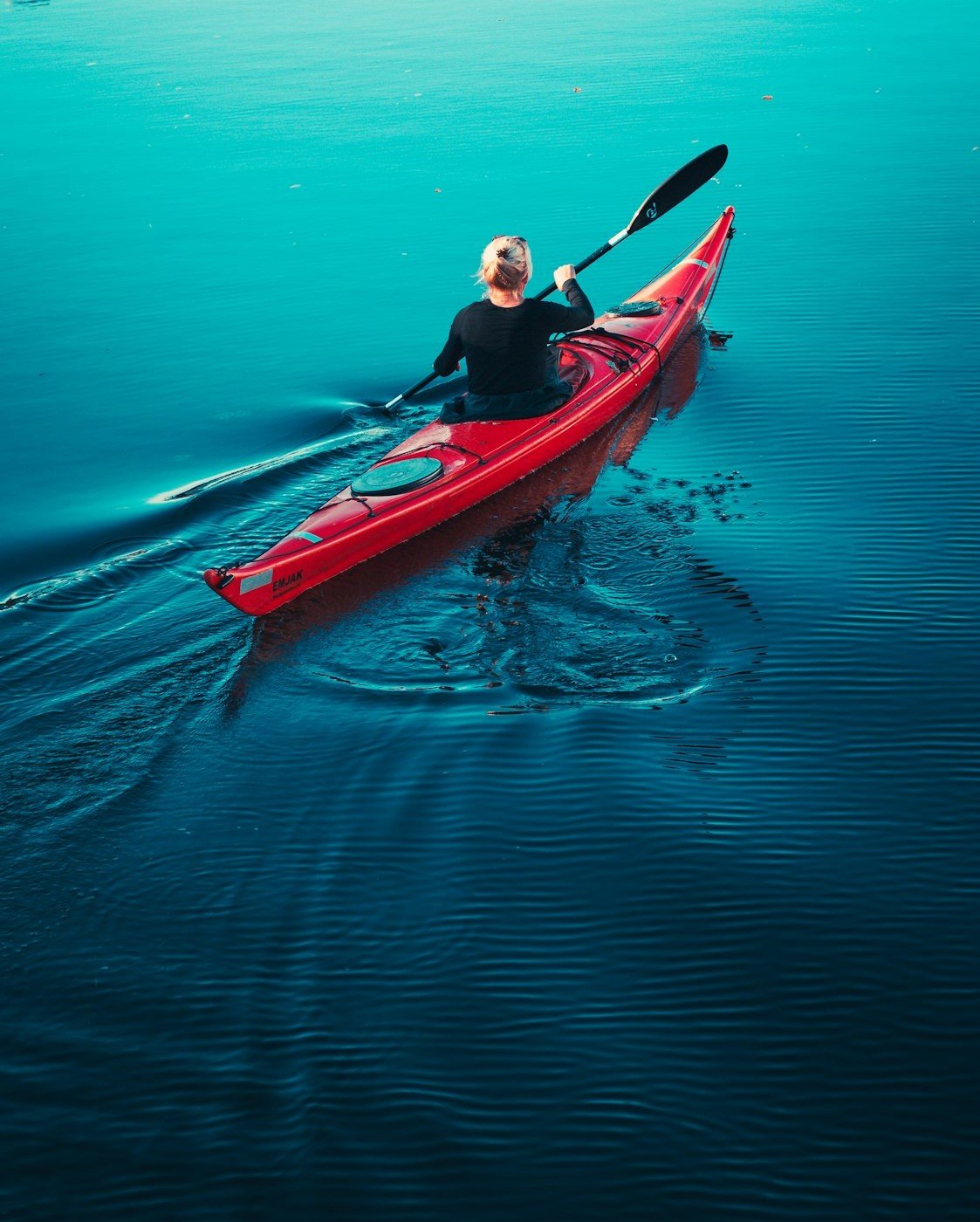 Une kayakiste glisse sur une mer d’huile, à la fin du jour