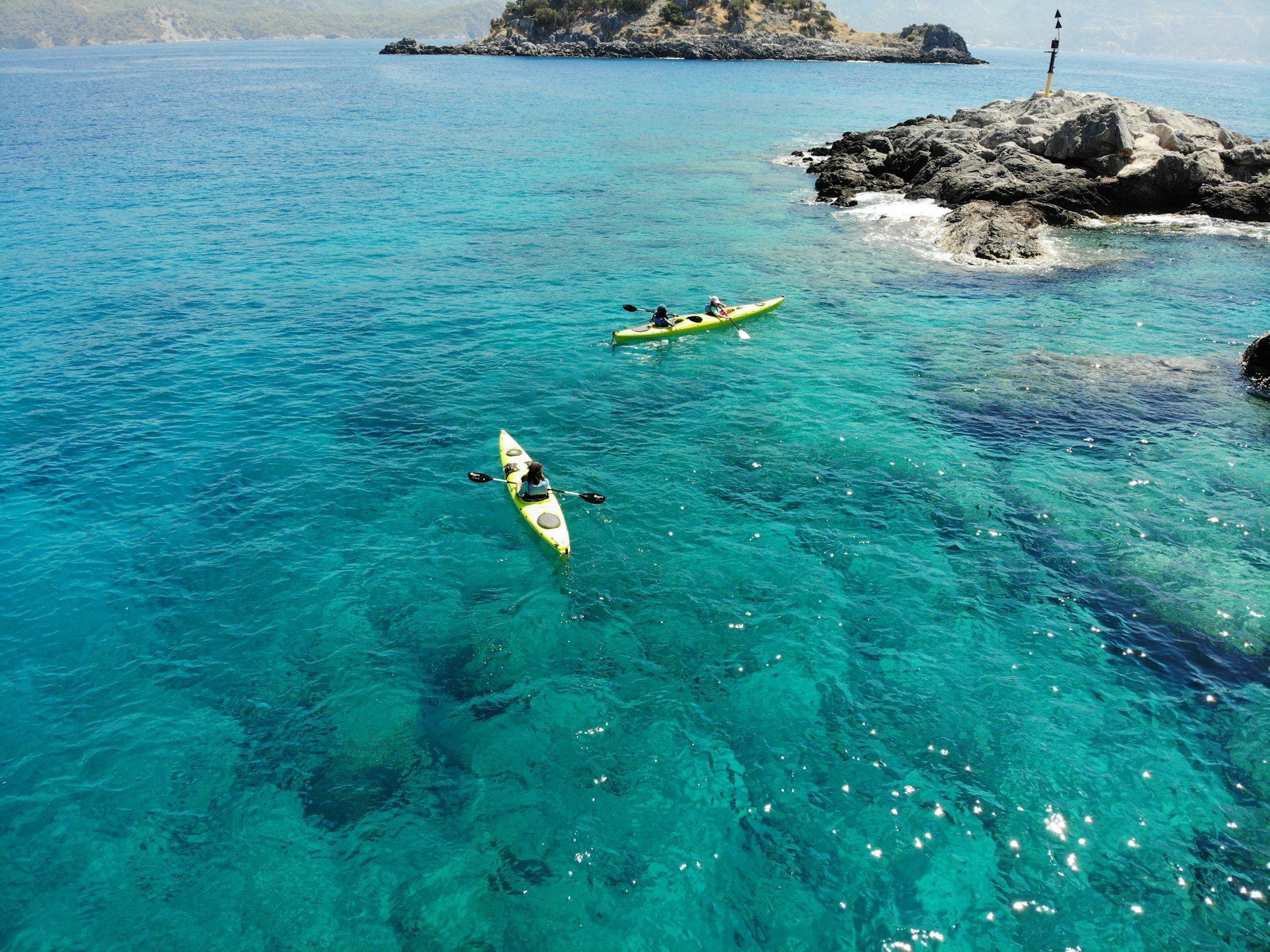 Deux kayaks de mer jaunes sur une eau turquoise, près d’un îlot rocheux
