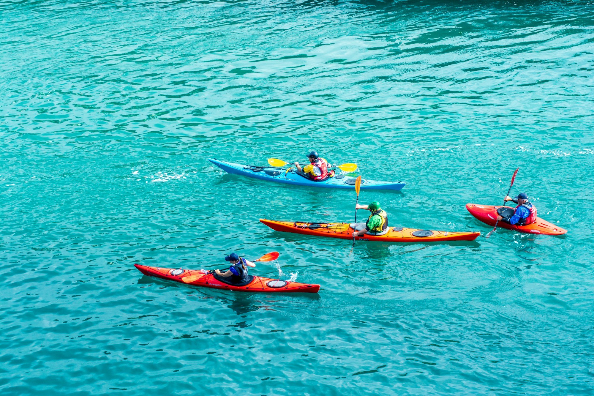 Quatre kayaks colorés naviguent ensemble sur une eau turquoise